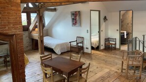 A cozy loft-style room with a wooden dining table and chairs, a bed with a white canopy, and a large mirror reflecting the room. - LE Gite DE Myans - Myans (MYANS)