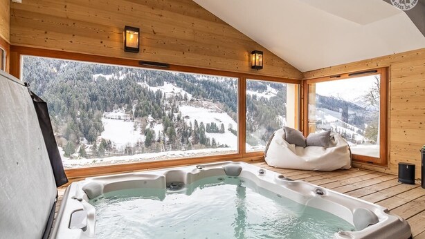 Eine Holzhütte mit Whirlpool und Sitzsack, mit Blick auf eine verschneite Berglandschaft.