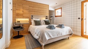 Ein Schlafzimmer mit einer Wand aus Holzverkleidung, einem Bett mit Kissen und gefalteten Handtüchern, einem Sessel und einem Nachttisch.