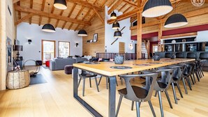 Ein geräumiger Essbereich mit einem langen Holztisch und modernen Stühlen, eine gemütliche Sitzecke mit Sofas und eine hohe Holzbalkendecke.