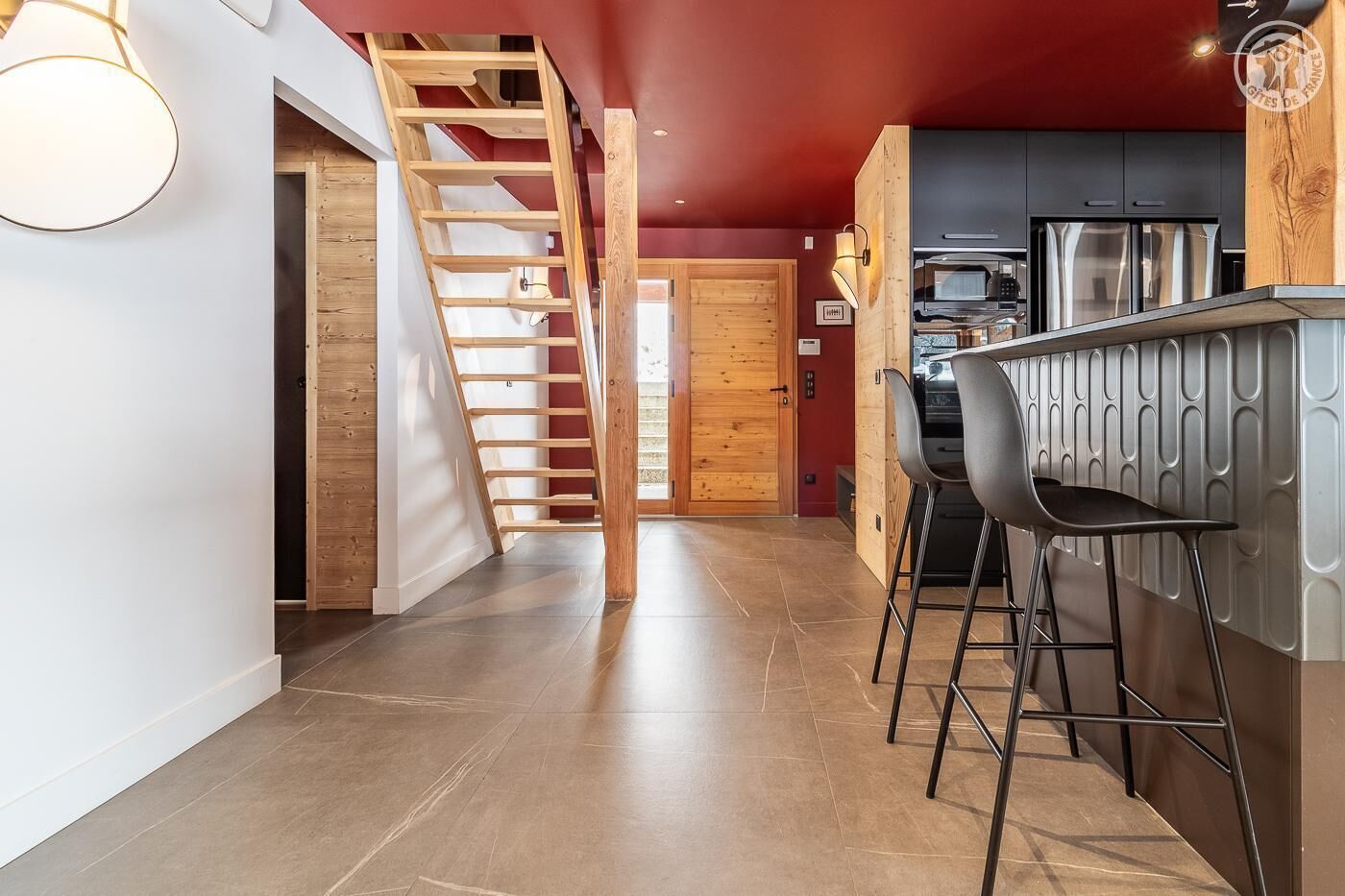A modern kitchen with a wooden staircase, a bar area, and a view into the dining room.