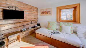 A cozy room with a wooden wall, a bed with pillows, a bedside table with a lamp, and a window. - Chalet Lidia Ski in-Ski out 50m (Livigno)
