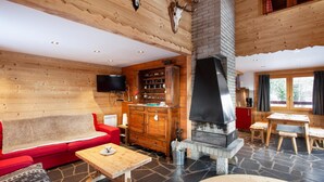 A cozy cabin interior with a fireplace, wooden walls, a red sofa, and a dining area. - LES Comognes - LA Rosiere-montvalezan (LA ROSIERE MONTVALEZAN)