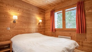 A wooden-paneled bedroom with a bed, two wall-mounted lamps, a window with red curtains, and a radiator. - LES Comognes - LA Rosiere-montvalezan (LA ROSIERE MONTVALEZAN)