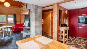 A cozy cabin interior with a stone fireplace, a dining area, a red kitchen, and a wooden ceiling. - LES Comognes - LA Rosiere-montvalezan (LA ROSIERE MONTVALEZAN)