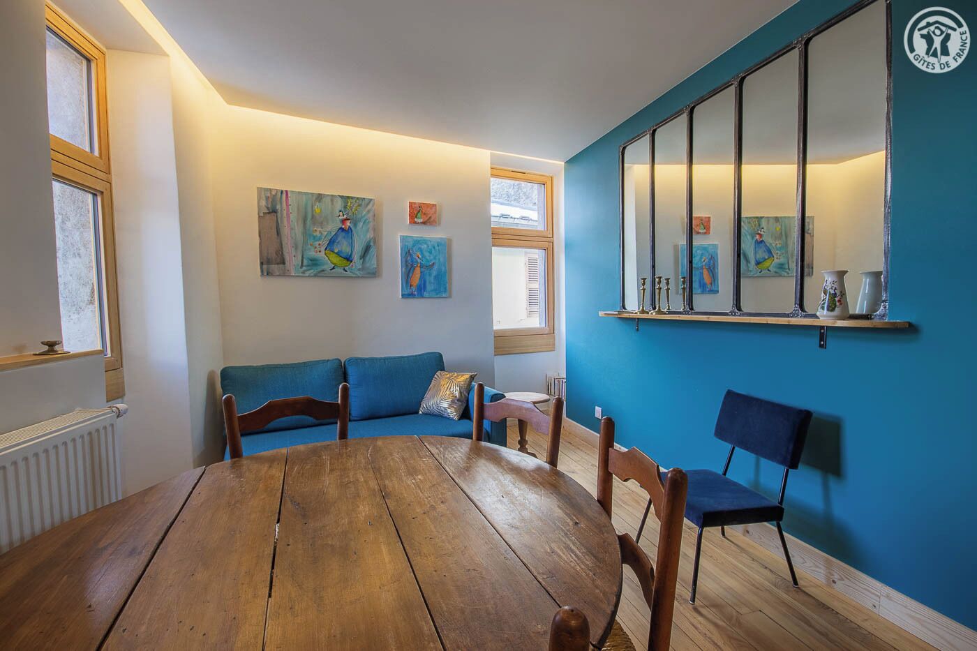 Una habitación con una mesa de madera, un sofá azul y cuadros en las paredes.