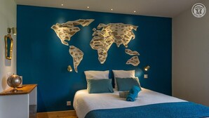 Een slaapkamer met een wereldkaart op de muur, een bed met blauw beddengoed, en een wereldbol op een nachtkastje.
