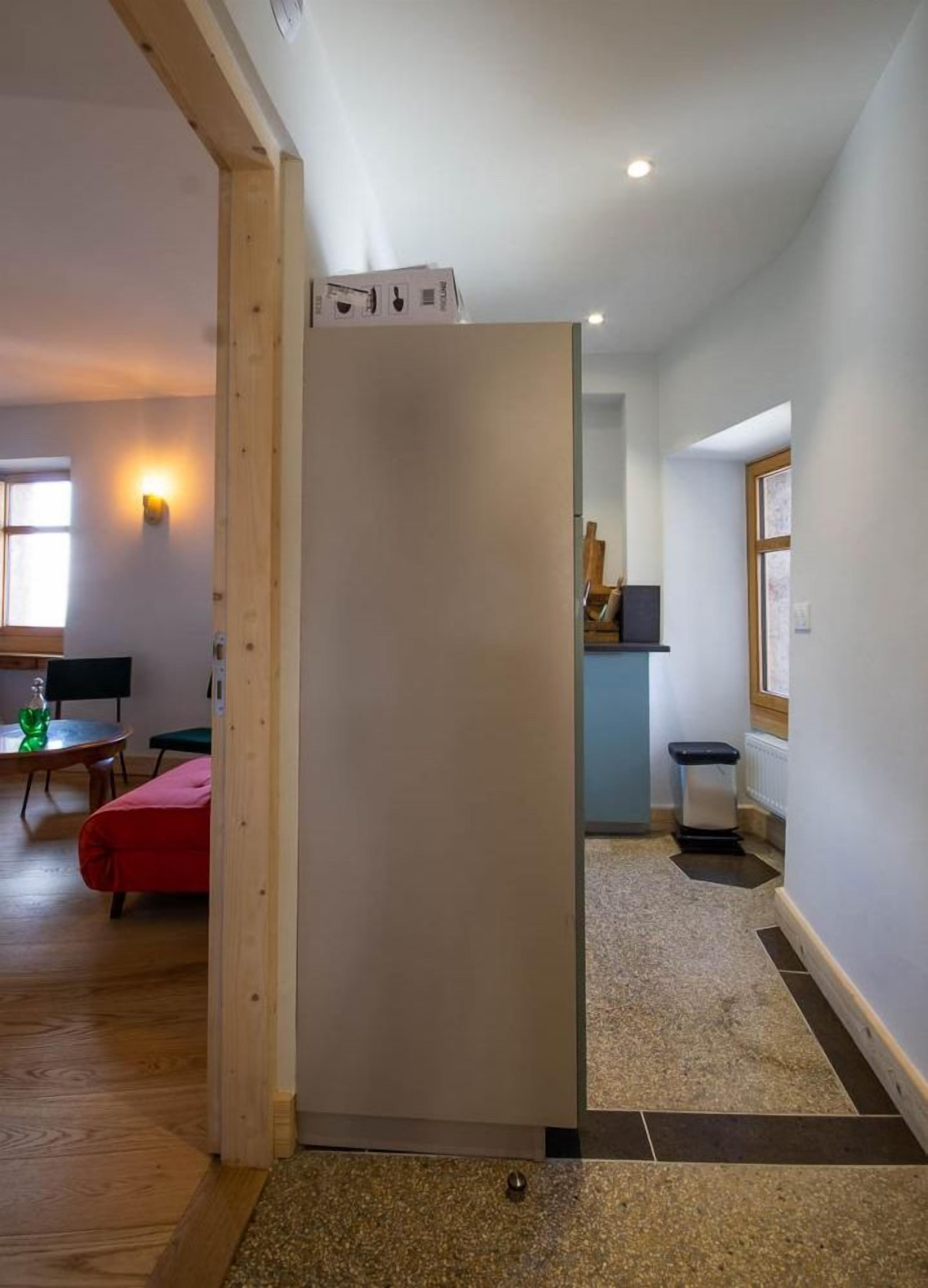 Un interno moderno con una porta in legno, una zona pranzo con tavolo e sedie, e un angolo cottura con finestra e bancone.