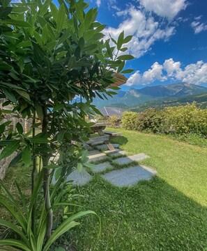 Un jardín con un sendero de piedra, abundante vegetación y montañas al fondo.