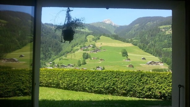 Vista desde una habitación con un amplio ventanal sobre un valle verde con casas y una montaña a lo lejos.