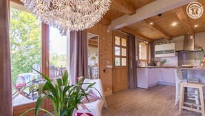 Um quarto acolhedor com teto de madeira, área de jantar com mesa e cadeiras, cozinha com bancada e armários, e uma janela grande com cortinas.