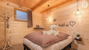 Um quarto de madeira acolhedor com uma cama, um ursinho de pelúcia, uma parede com um símbolo de coração e uma pequena prateleira.