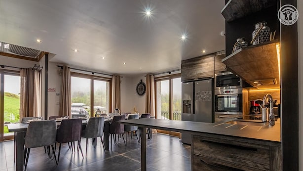 A modern kitchen with a central island, stainless steel appliances, and a dining area with a view. - Hislianie - LES Belleville (LES BELLEVILLE)