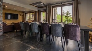 A dining area with a long table, multiple chairs, a television, and a stone wall. - Hislianie - LES Belleville (LES BELLEVILLE)