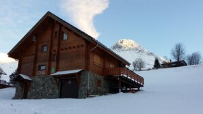 Un chalet en bois avec des fondations en pierre, un balcon et une vue sur les montagnes.