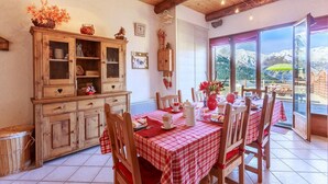 Comedor con mantel a cuadros, sillas de madera y vistas a las montañas a través de grandes ventanales.