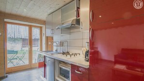 Une cuisine de taille réduite, avec un meuble rouge, une hotte en acier inoxydable et un lave-vaisselle.