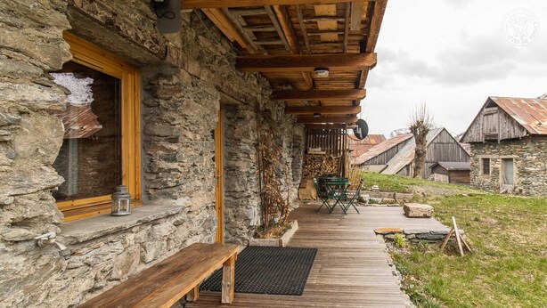 Un bâtiment rustique en pierre, doté d’une terrasse en bois, d’un banc et d’une table.