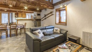 A cozy living room with a leather sofa, a dining table with chairs, and a kitchen area in the background.