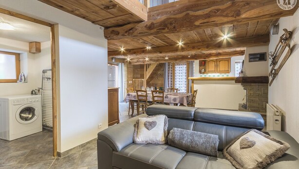 A cozy living room with a sofa, a washing machine, and a dining area with a table and chairs.