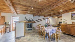 A rustic interior with a stone fireplace, wooden dining table, and a kitchen area.