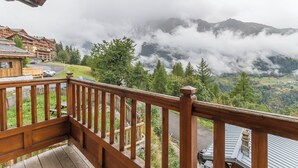 A wooden balcony overlooking a mountainous landscape with a view of a lodge and a road.