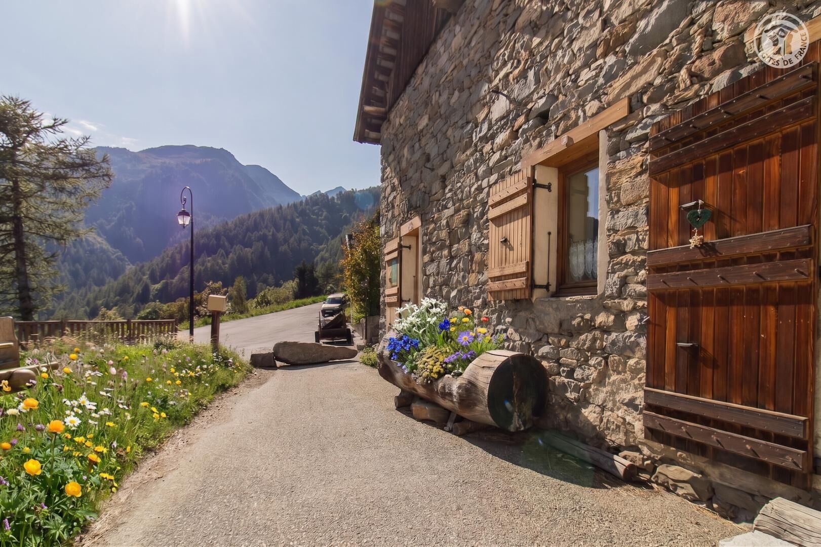 A stone building with wooden shutters and a flower bed in front.