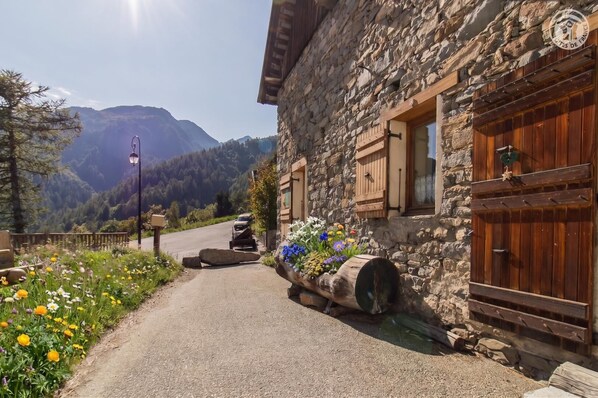 A stone building with wooden shutters and a flower bed in front.