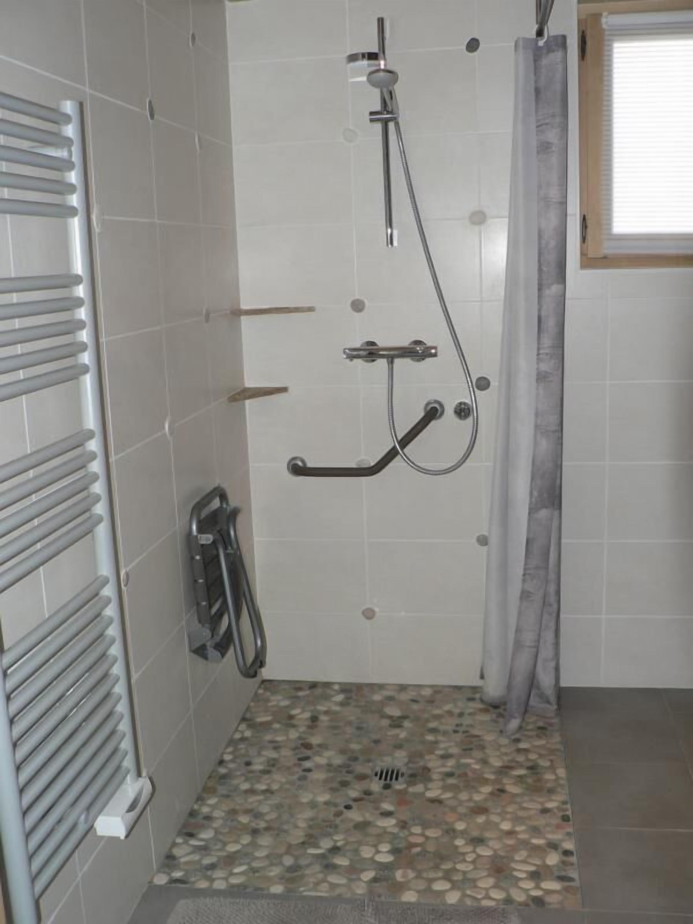 A shower area with a tiled floor, a showerhead, and a handrail.