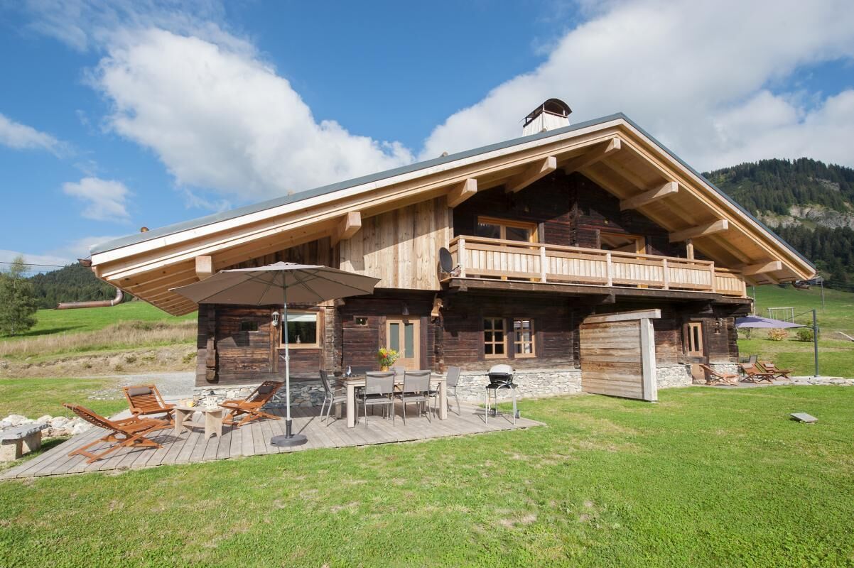 Une cabane en bois dotée d’un balcon, d’un espace extérieur aménagé pour s’asseoir et de fondations en pierre.