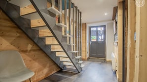 A modern interior with a wooden staircase, a grey chair, and a door leading outside.