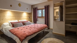 A bedroom with a wooden headboard, a large bed with multiple pillows, a window with curtains, and a built-in wardrobe.