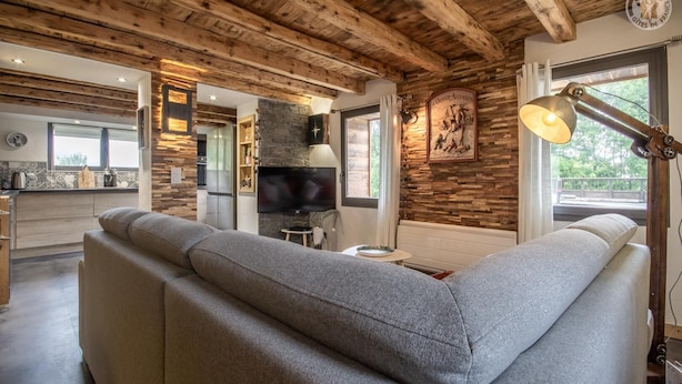 A modern living room with a grey sectional sofa, a flat-screen TV, and a stone fireplace.