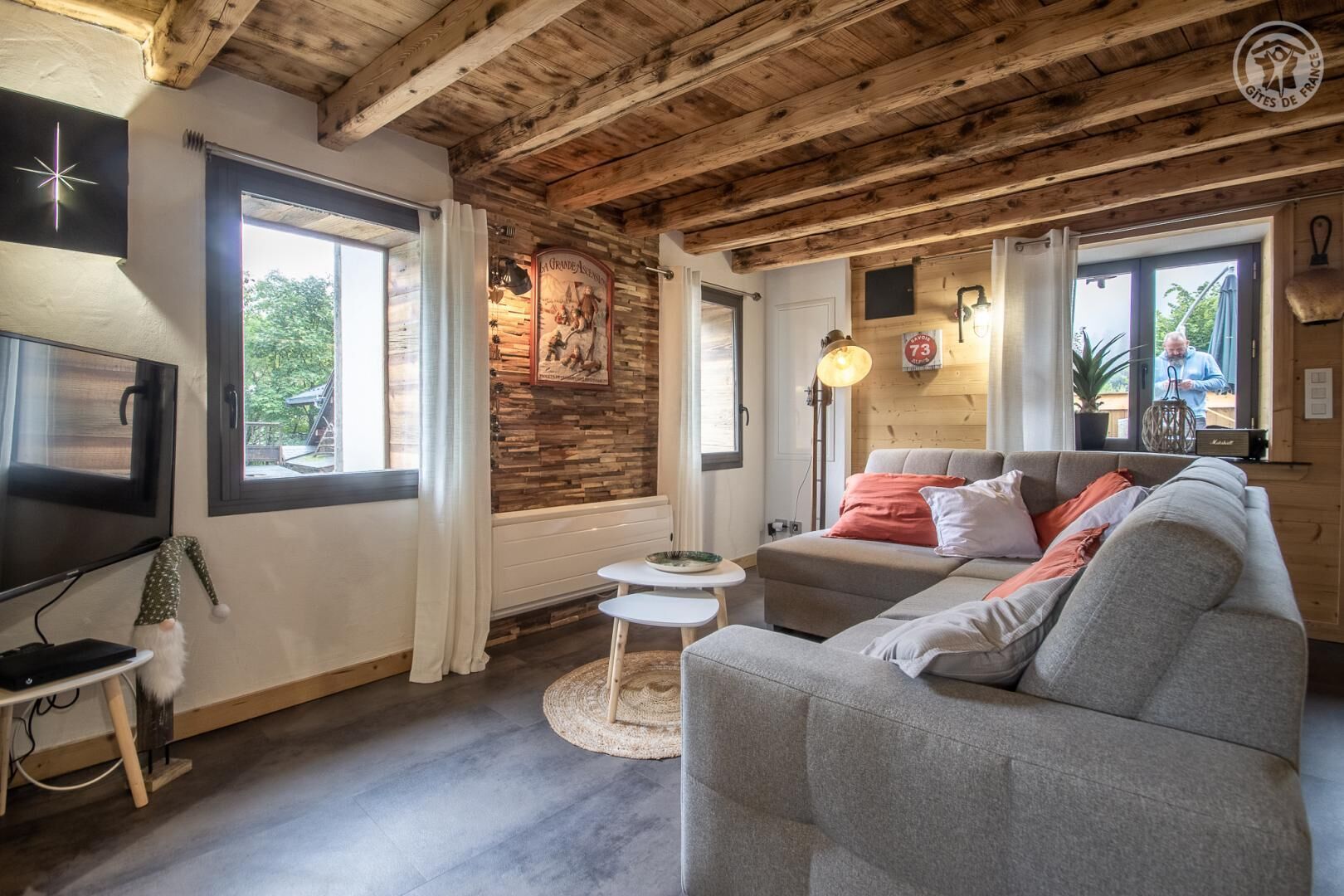 Un salón acogedor con un sofá gris, una mesita redonda, un televisor y una pared de piedra.