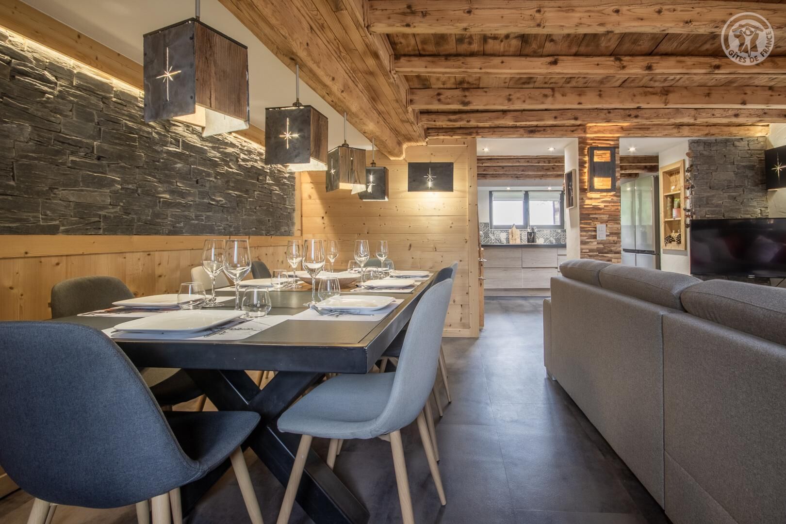 A dining area with a wooden table set for six, flanked by blue chairs, and a grey sofa in the background.