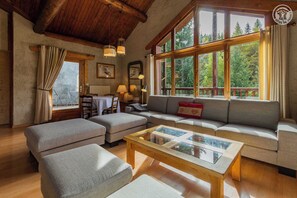 Una sala de estar acogedora con un ventanal, un sofá, dos sillones, una mesa de centro y una zona de comedor con mesa y sillas.
