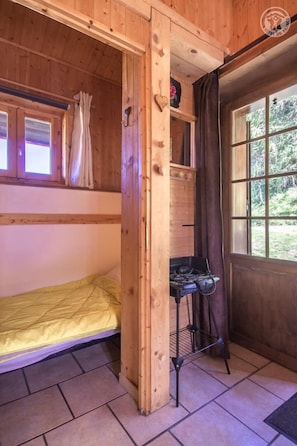 Eine Holzhütte mit Etagenbett, einer kleinen Küchenzeile und einem Fenster mit Vorhängen.