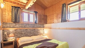 Una habitación acogedora de madera con una cama, pared de piedra y dos ventanas con cortinas.