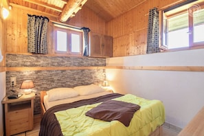 Ein gemütlicher Holzraum mit Bett, Steinwand und zwei mit Vorhängen versehenen Fenstern.