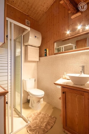 Ein Badezimmer mit Holzwandverkleidung, einer Glasdusche, einer weißen Toilette, einem Waschbecken und einem Spiegel.