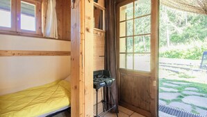 Una cabaña de madera con una cama individual, una pequeña cocina y un ventanal con vistas al exterior.