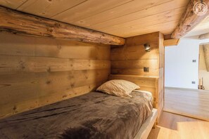Una habitación tipo cabaña de madera con una cama individual, paredes de madera y techo inclinado.