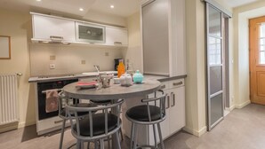Cocina compacta con una mesa redonda de comedor, dos taburetes de bar, un microondas y una tetera.