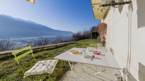 Una mesa con vistas a un valle y montañas, un banco verde y un mantel blanco.