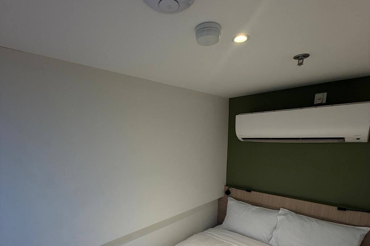 Une chambre d’hôtel équipée d’un lit, d’un climatiseur fixé au mur et d’un luminaire au plafond.