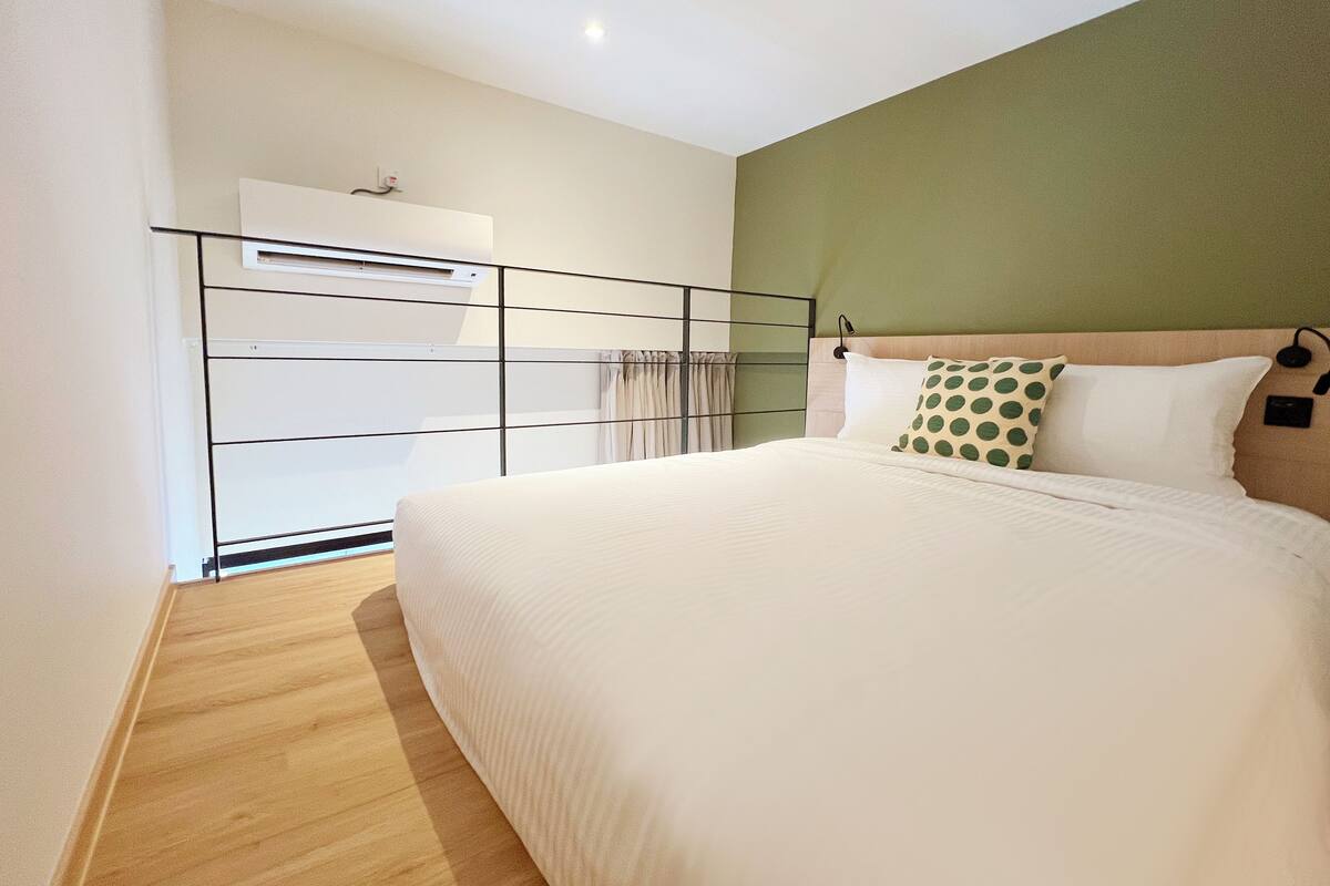 Une chambre moderne avec un grand lit, un système de climatisation intégré, un plancher en bois et un mur d’accent de couleur verte.