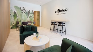 Un intérieur moderne avec un canapé vert, une table ronde agrémentée d’une plante et un mur sur lequel on peut lire le texte suivant : « Coluwoo City Living, votre style de vie ».