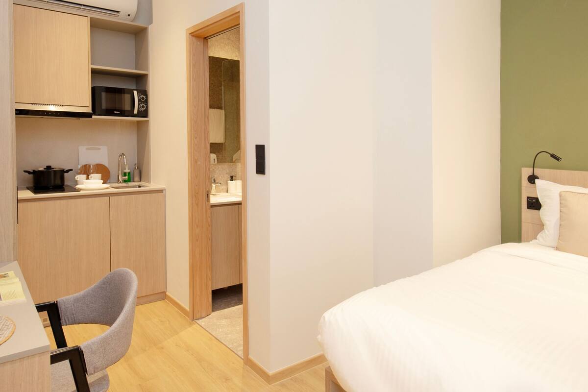 Une chambre d’hôtel compacte comprenant un coin cuisine, un lit simple et un petit bureau avec une chaise.