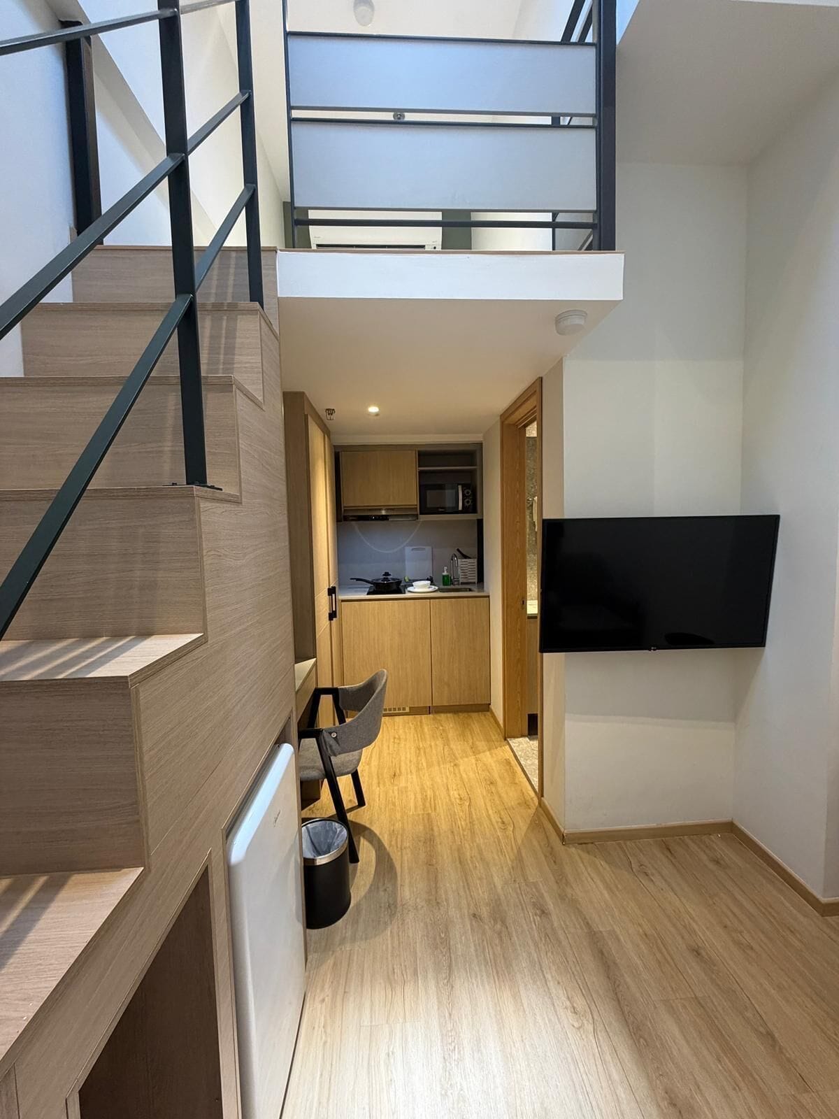 A modern apartment with a staircase, a kitchen, a dining area, and a TV mounted on the wall.