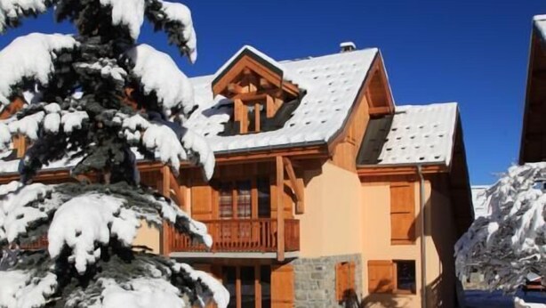 A wooden chalet with a stone entrance, surrounded by snow-covered trees and a clear blue sky. - LA Ferme DES Moulins (VALLOIRE)